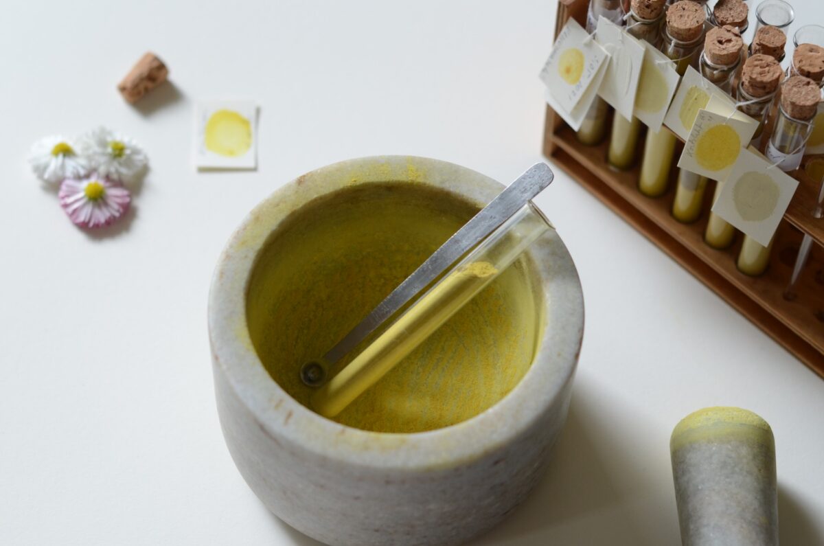 Kivist uhmris on kollane pigment; kõrval on pigmendiproovid klaastorudes ja lilled.